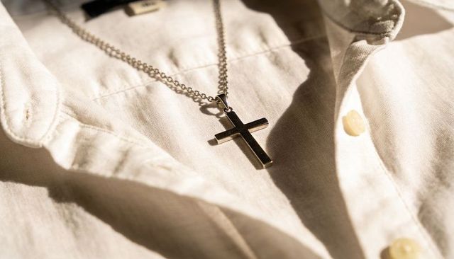 Gunmetal cross necklace resting on cream linen shirt collar reflecting warm sunlight