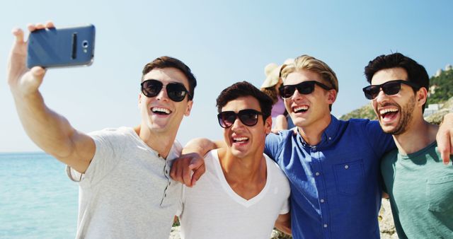Group of young friends wearing casual outfits and sunglasses, taking a selfie at the beach during a bright, sunny day. Perfect for depicting themes of friendship, vacation, summer fun, youth culture, social connection and outdoor activities.