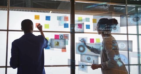 Women collaborating on glass wall sketching sticky notes and code overlays for ux planning