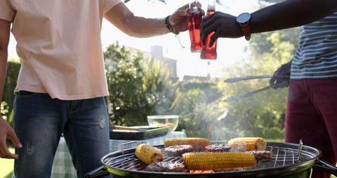 Friends Enjoying Outdoor Barbecue with Drinks and Grilling Foods