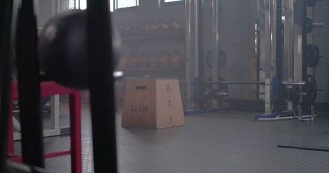 Wooden plyometric box sitting on rubber gym floor near power rack and kettlebells