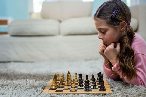 Young girl deeply engaged in chess strategy on cozy carpet