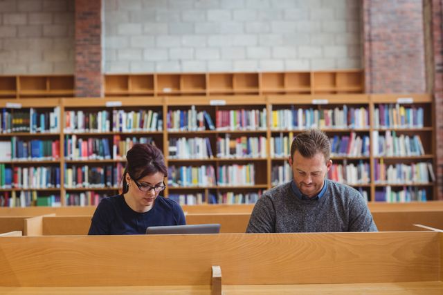 Mature students using laptop to help with studying in college library