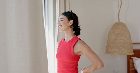 Happy woman in red tank top relaxing by bright window