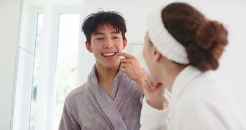 Morning rituals: diverse couple smiling at mirror in robes sharing intimate dental moment