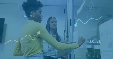 Two women collaborating on glass whiteboard with analytics overlay in modern workspace