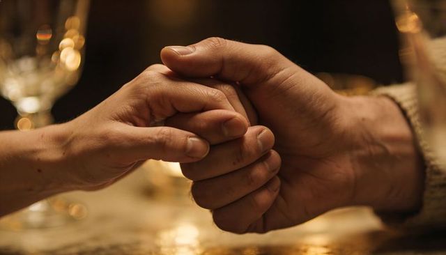 Holding hands at candlelit dinner closeup showing comfort, warmth and intimacy