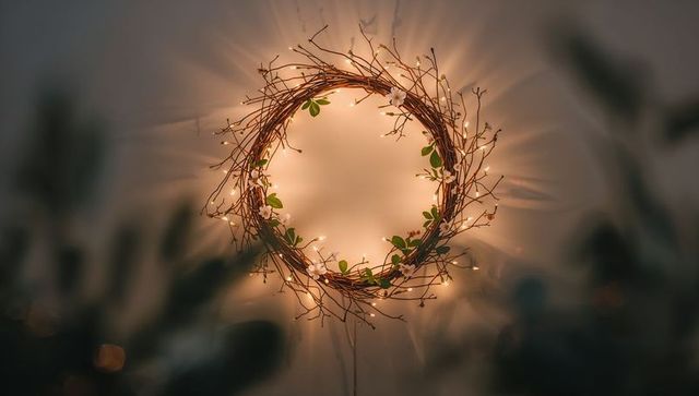 Glowing twig wreath with warm fairy lights and blossoms on neutral wall for cozy interior