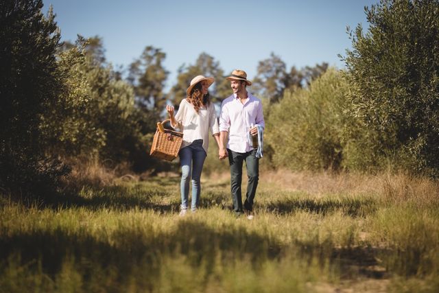 Young couple holding hands while carrying picnic basket at olive farm