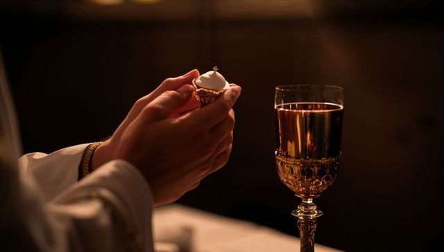 Clergy holding communion wafer elevating over ornate gold chalice during eucharist