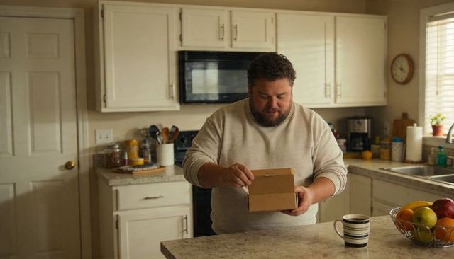 Man inspecting and opening box at cozy kitchen island with coffee mug and fruit bowl
