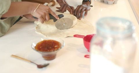 African american couple trimming rolled dough with pizza cutter, collaborating in kitchen