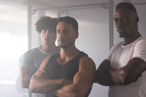 Three diverse male athletes standing shoulder-to-shoulder in gym demonstrating teamwork, strength