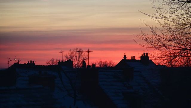 Sunset Silhouetted Rooftops with Chimneys and Antennas over Snowy Twilight Sky