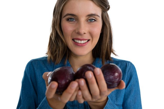 Portrait of young woman holding plums while standing against white background