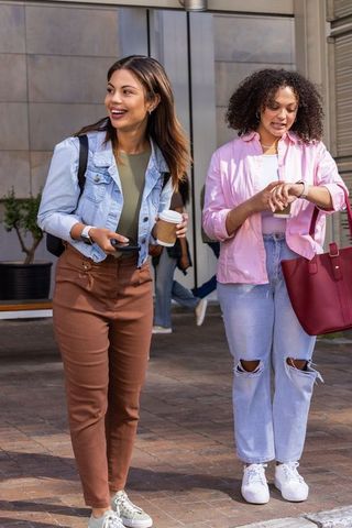 Two women walking through urban plaza holding coffee and smartphone, checking watch