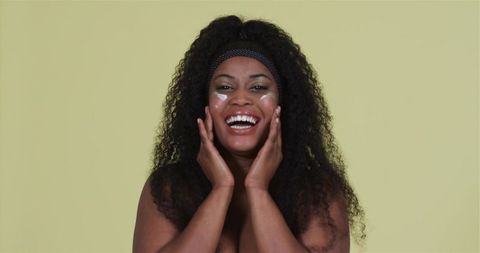 Joyful black woman enjoying skincare routine with headband