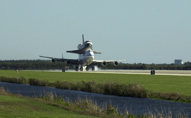 Historic moment captured as Shuttle Carrier Aircraft lands carrying the orbiter Columbia at Kennedy Space Center. Suitable for use in articles, documentaries, or educational materials focused on space exploration, aviation, NASA missions, or the history of the space shuttle program. Highlights Columbia's return after 17 months of modification and refurbishment.