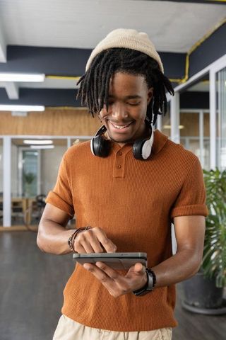 African american man smiling while using tablet in modern coworking space with headphones