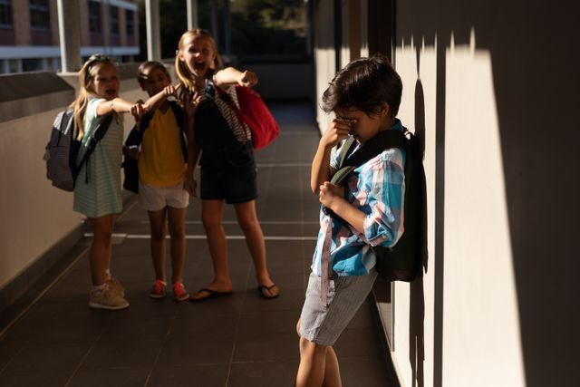 This image depicts a group of school children bullying a crying boy in a hallway. The boy is standing against the wall, covering his face, while the other children are pointing and teasing him. This image can be used in articles or campaigns addressing bullying, emotional distress, and the importance of creating a safe school environment. It can also be used in educational materials to raise awareness about the impact of bullying on children.