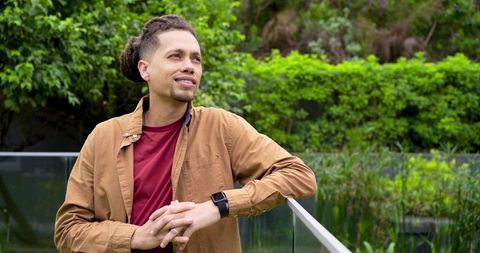 Man in 30s leaning on glass railing at botanical garden, contemplating amid lush greenery