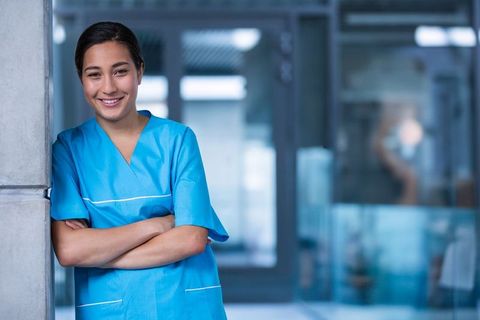 Nurse in Blue Scrubs Leaning in Hospital Corridor, Smiling with Confidence - Download Free Stock Images Pikwizard.com
