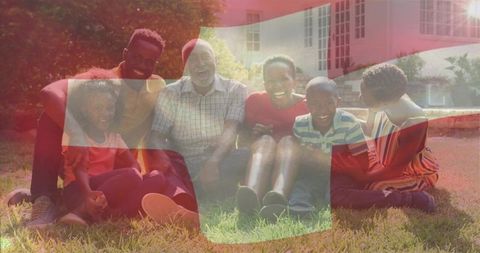 Multigenerational family sitting and smiling on sunlit front lawn with flag overlay