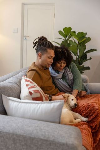 Couple cuddling on sofa with sleeping puppy and warm blanket, cozy home togetherness