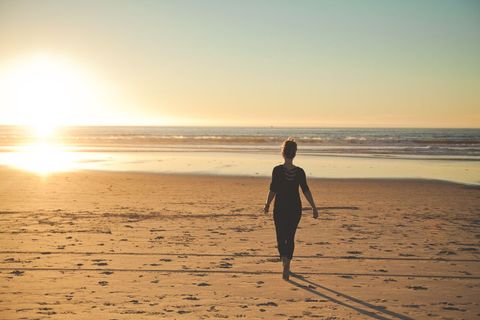 Woman Walking Towards Sunset on Sandy Beach