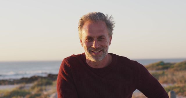 Middle-aged man with a gray hair smiling at the beach during sunset. Use for concepts related to relaxation, outdoor recreation, lifestyle, or travel advertising. Ideal for promoting coastal tourism, mental well-being, or active retirement lifestyle.