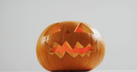 Glowing jack-o-lantern with jagged teeth sitting on minimal white surface for halloween