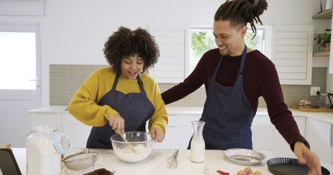 African american couple baking together in bright kitchen, stirring batter, sharing joy