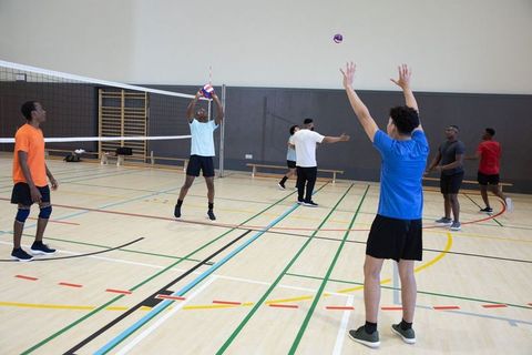 Indoor volleyball players practicing set and serve drills on marked gym court during club training