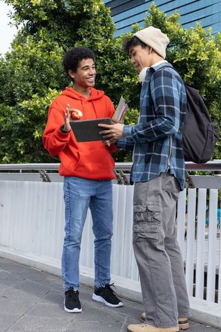 Multicultural college students collaborating outdoors with tablet and notebooks, smiling