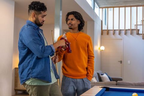 Friends clinking bottles by blue-felt pool table in contemporary home game room