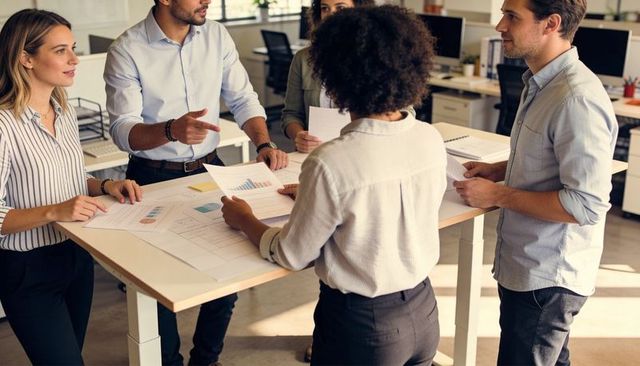 Collaborative team reviewing business charts around standing desk in modern open office