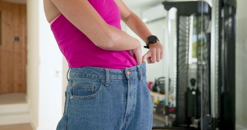 Person in jeans showing weight loss on indoor gym background