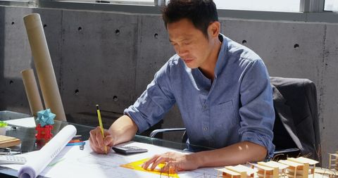 Asian Architect Working on Blueprint with Set Square in Office