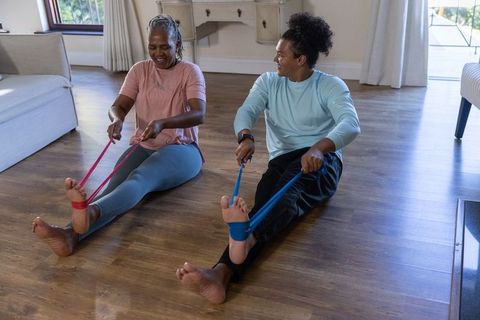 Senior african american woman and young man stretching legs with resistance bands at home