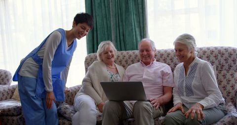 Seniors enjoying time with nurse, using laptop in nursing home