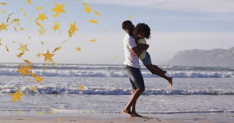 Father lifting daughter on sunlit beach with gold star confetti and rolling waves