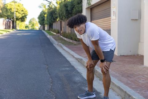 African american man catching breath after run on quiet suburban street wearing smartwatch
