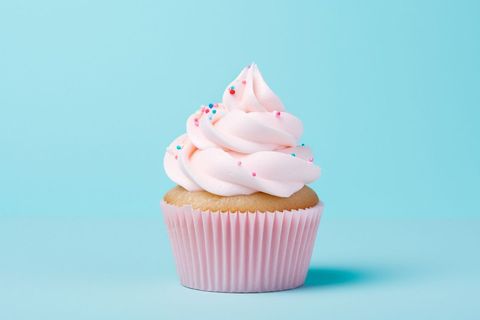 Vanilla cupcake with pink frosting and sprinkles on blue background