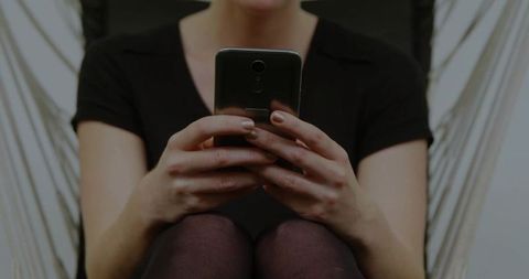 Woman Relaxing at Home Using Smartphone in Hanging Chair