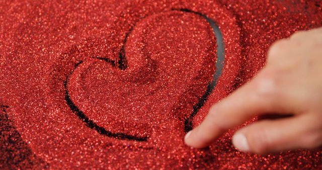 Person drawing shape of heart on red glitter. Scattered red glitter on surface 4k