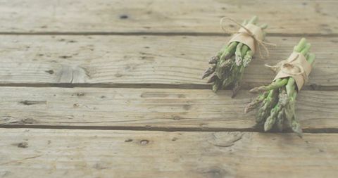 Bundling asparagus bunches on rustic wooden plank, tying twine and kraft wraps, copy space