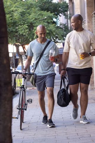 African american men walking with bicycle and drinks on city sidewalk