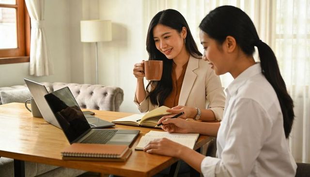 Female colleagues collaborating in home office with laptops, notebooks and coffee