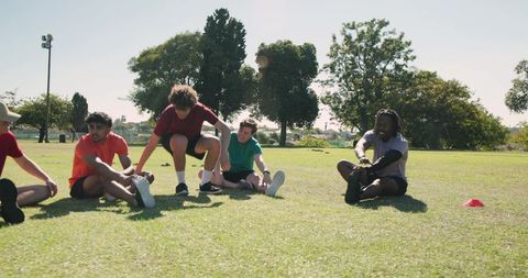 Diverse young men stretching in sunny park before group training session, outdoor fitness