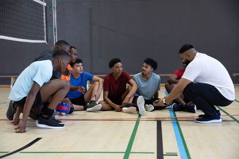 Diverse youth volleyball team huddle receiving coaching and strategy in indoor gymnasium